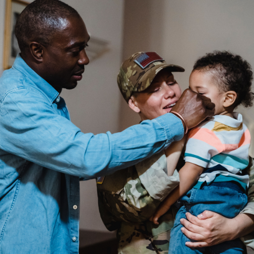 Mom in military uniform holding her child, dad in plain clothes wiping child's face